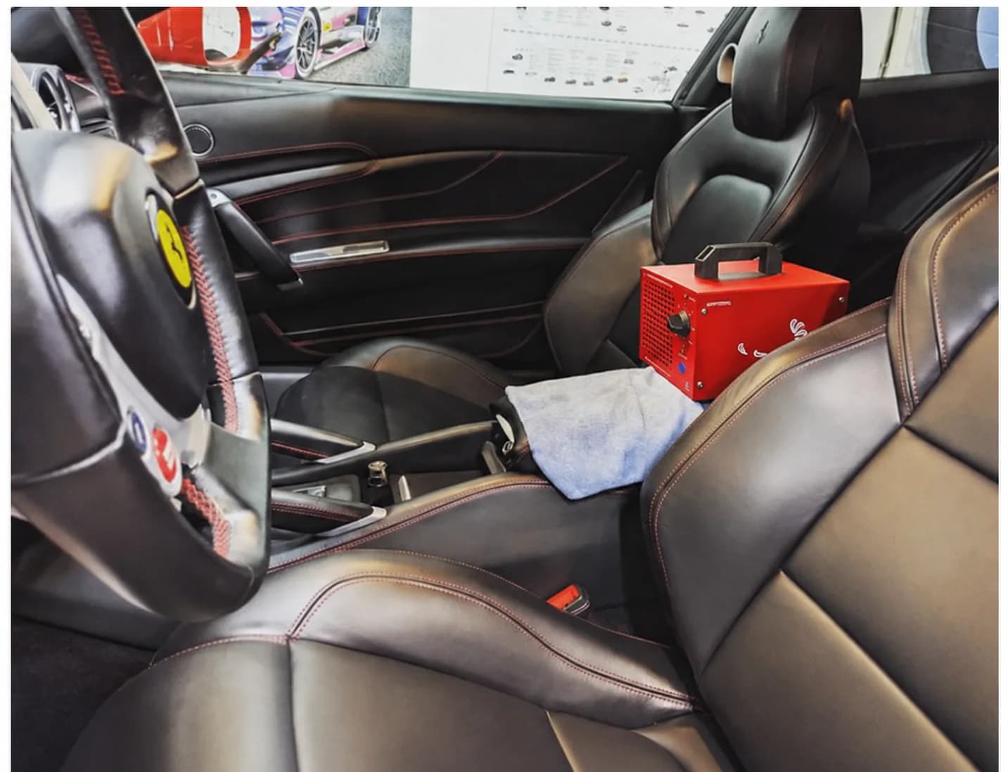 Ferrari black leather interior with a red ozone generator set on a towel for car odor treatment
